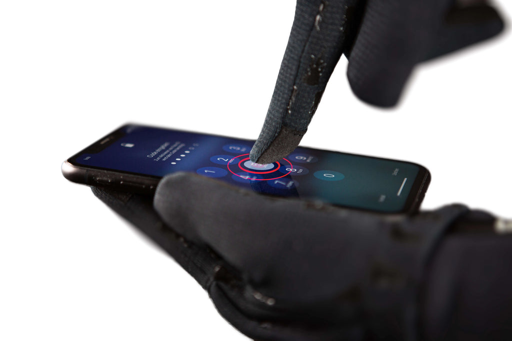 A person wearing Windpro Liner gloves by The Heat Company using a smartphone with a dark screen.