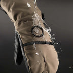 Brown waterproof glove Shell with water splashing onto it against a dark background.