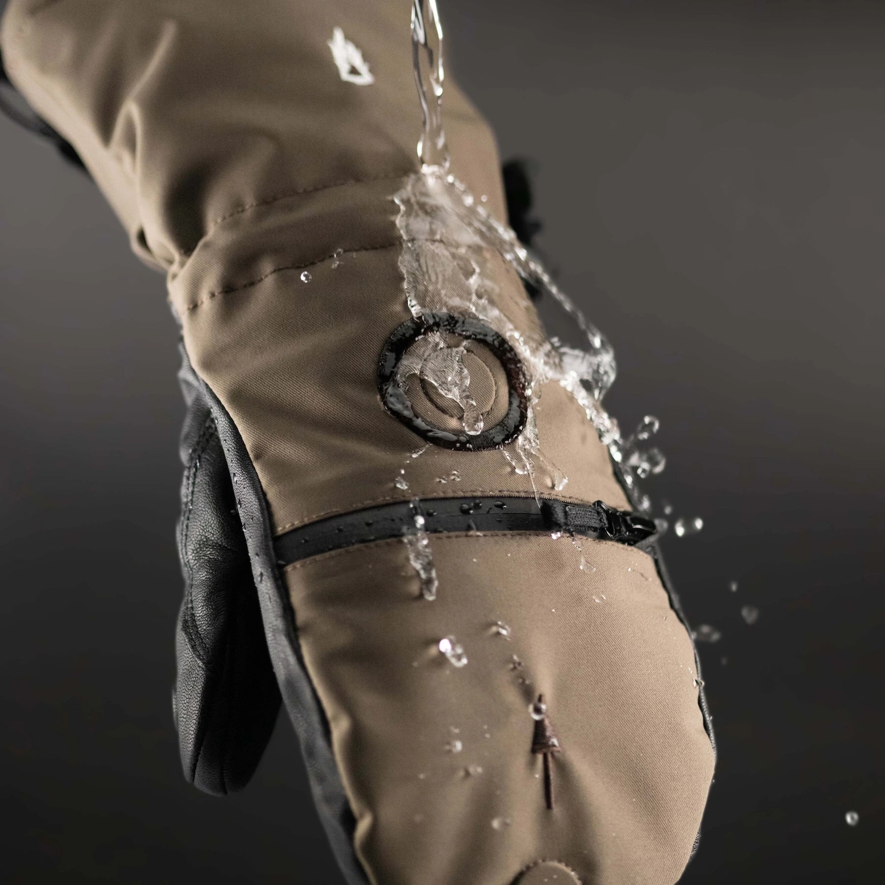Brown waterproof glove Shell with water splashing onto it against a dark background.